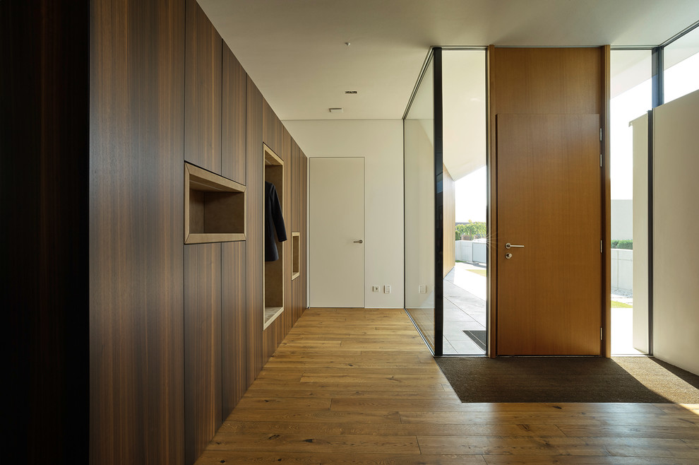 На фото: узкая прихожая в стиле модернизм с белыми стенами, паркетным полом среднего тона, одностворчатой входной дверью и входной дверью из дерева среднего тона с