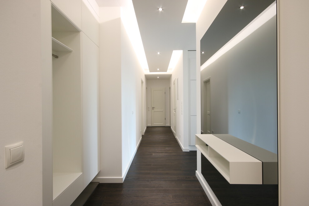 Immagine di un corridoio moderno di medie dimensioni con pareti bianche, parquet scuro, una porta singola, una porta bianca e pavimento marrone