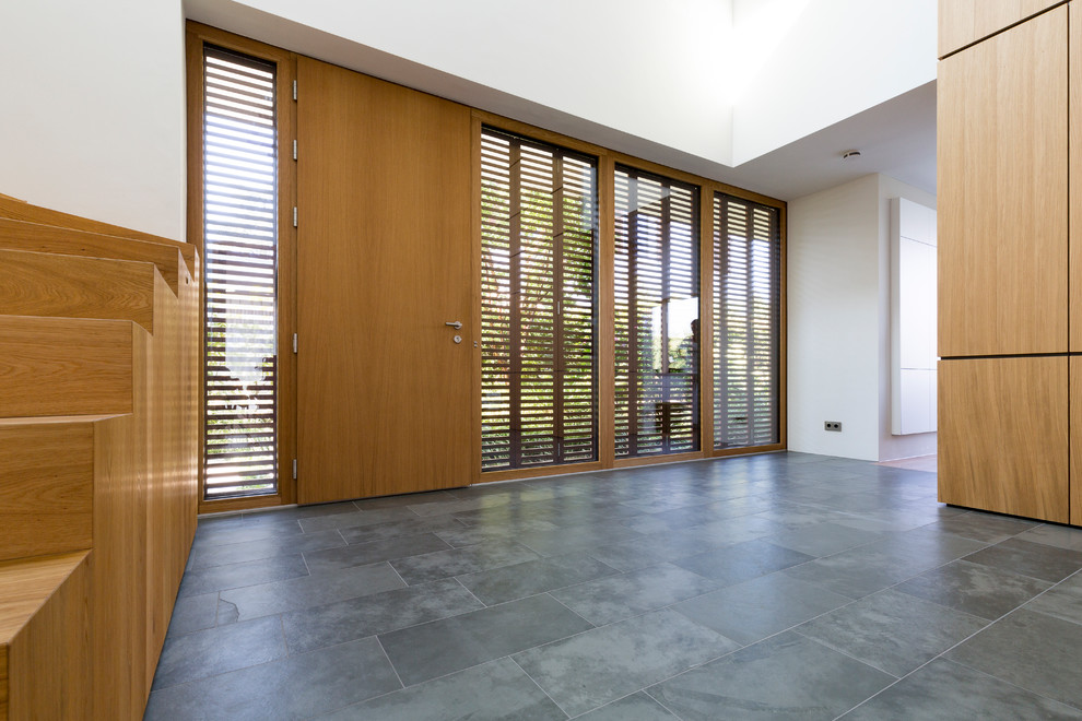 Idee per un grande ingresso minimalista con pareti bianche, pavimento in ardesia, una porta singola, una porta in legno bruno e pavimento grigio