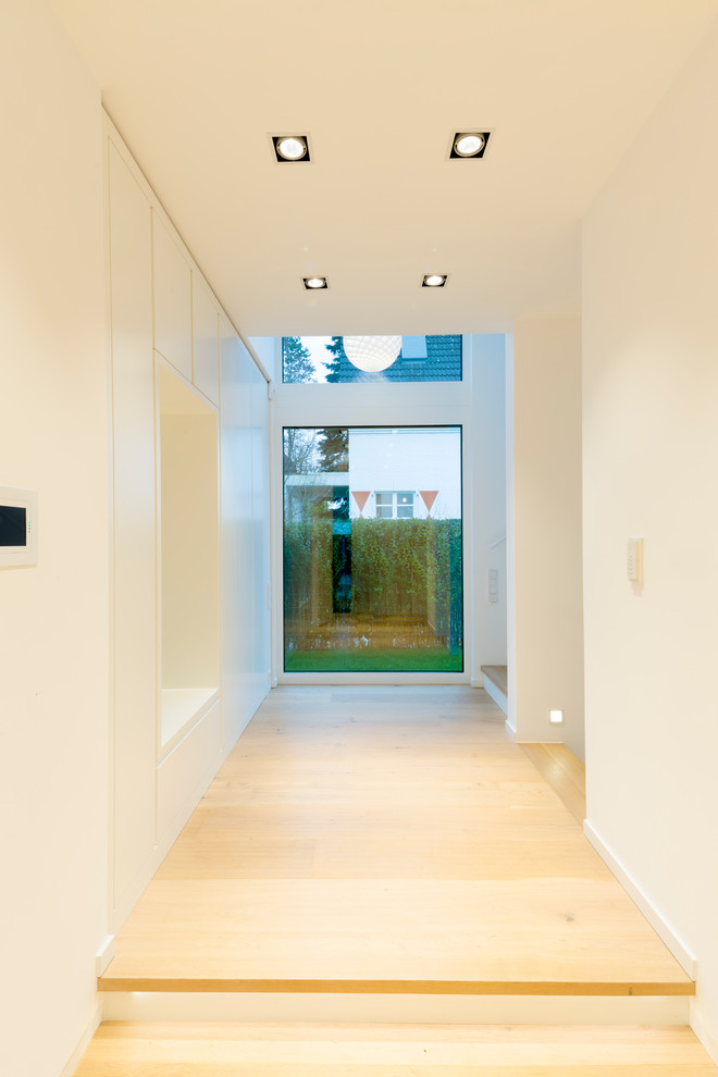 Imagen de distribuidor actual grande con paredes blancas, suelo de madera clara, puerta simple, puerta negra y suelo beige
