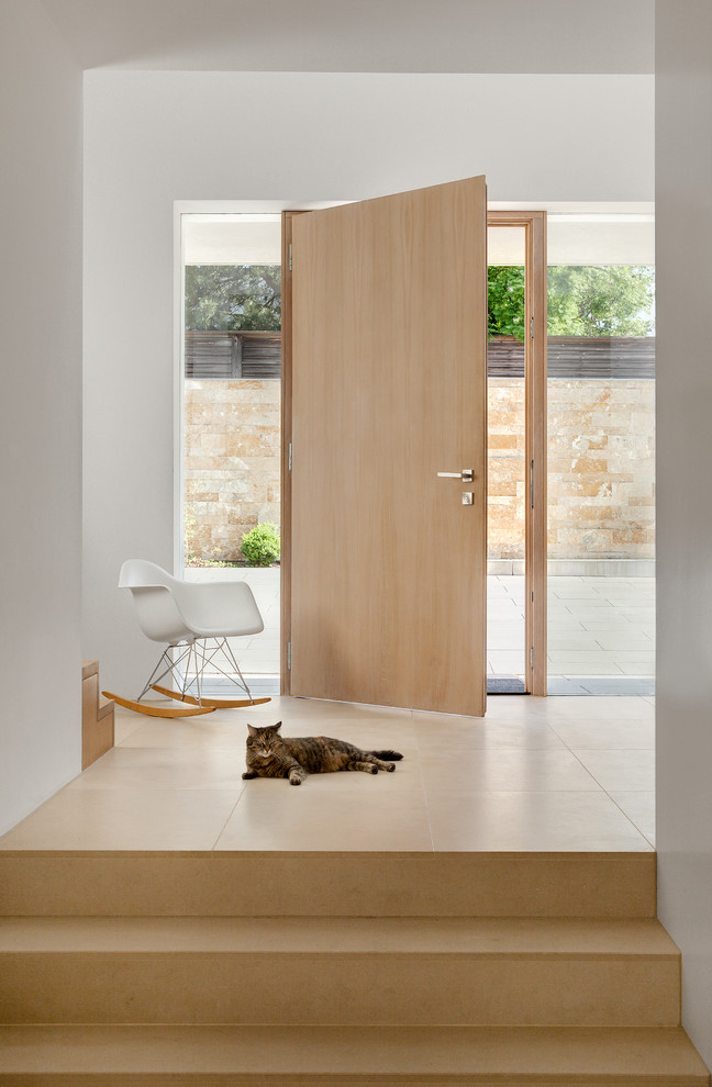 Cette photo montre un hall d'entrée moderne avec une porte simple, un mur blanc, un sol en travertin et une porte en bois clair.