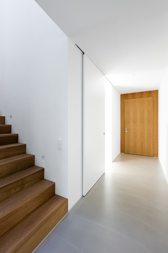 Immagine di un corridoio moderno di medie dimensioni con pareti bianche, pavimento in cemento, una porta singola, una porta in legno bruno e pavimento grigio