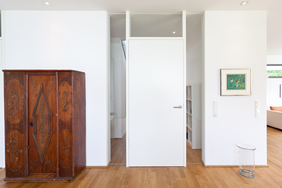Cette image montre un hall d'entrée design de taille moyenne avec un mur blanc, parquet clair, une porte simple et une porte blanche.