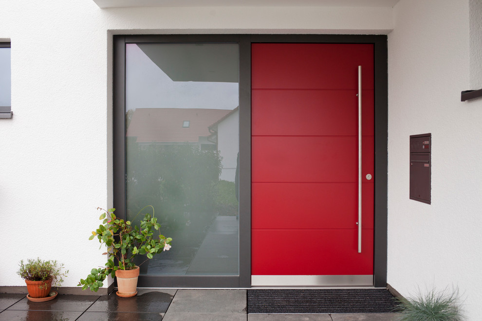 Imagen de puerta principal actual con paredes blancas, puerta simple, puerta roja y suelo de cemento