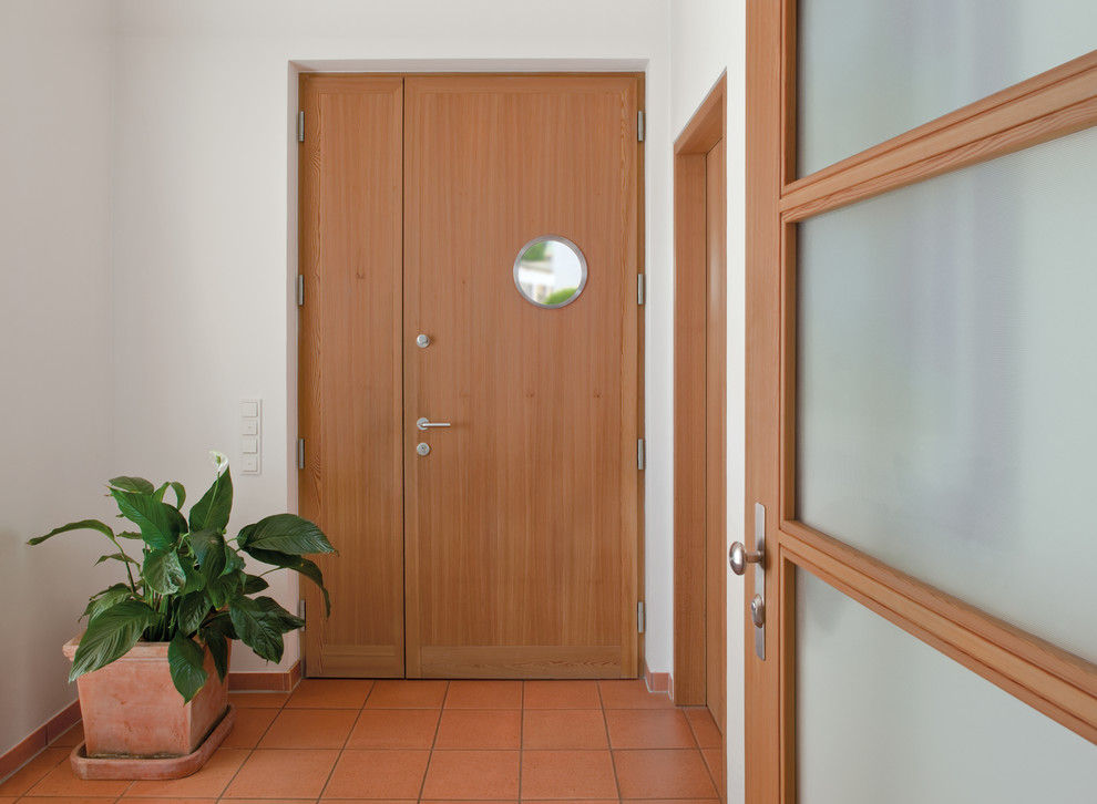 Diseño de puerta principal moderna de tamaño medio con paredes blancas, suelo de baldosas de terracota, puerta simple y puerta de madera clara