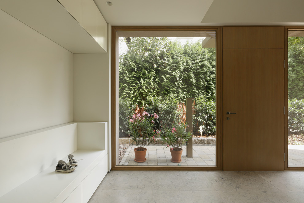 Photo of a medium sized contemporary boot room in Frankfurt with white walls, a single front door, a medium wood front door and limestone flooring.