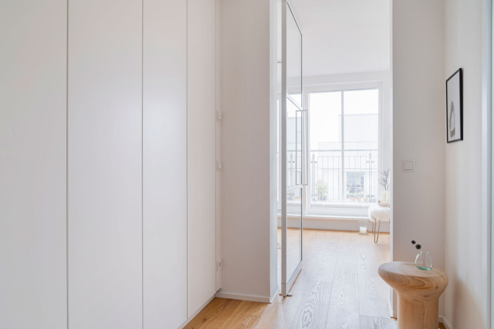 Modelo de entrada minimalista con paredes blancas, suelo de madera clara y suelo beige
