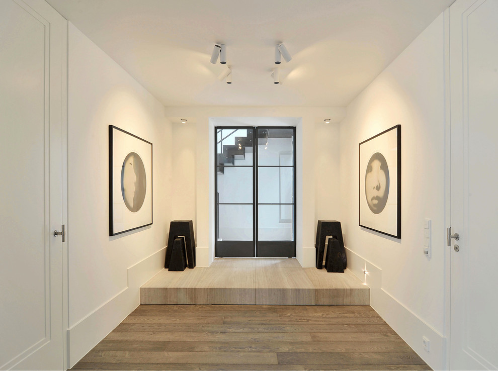Immagine di un corridoio minimalista di medie dimensioni con pareti bianche, pavimento in legno massello medio, una porta a due ante e una porta in vetro