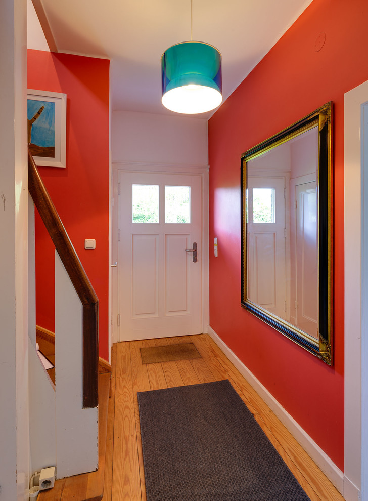 Ejemplo de hall actual de tamaño medio con paredes rojas, suelo de madera en tonos medios, puerta simple y puerta blanca