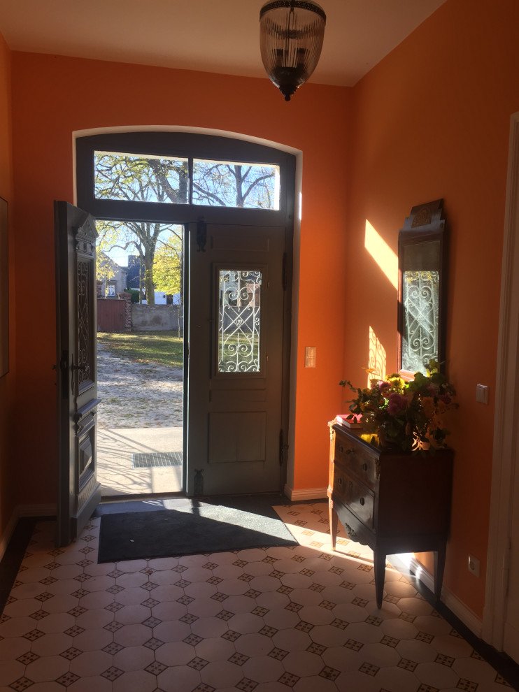 Immagine di un ingresso di medie dimensioni con pareti arancioni, pavimento in gres porcellanato, una porta a due ante e una porta marrone