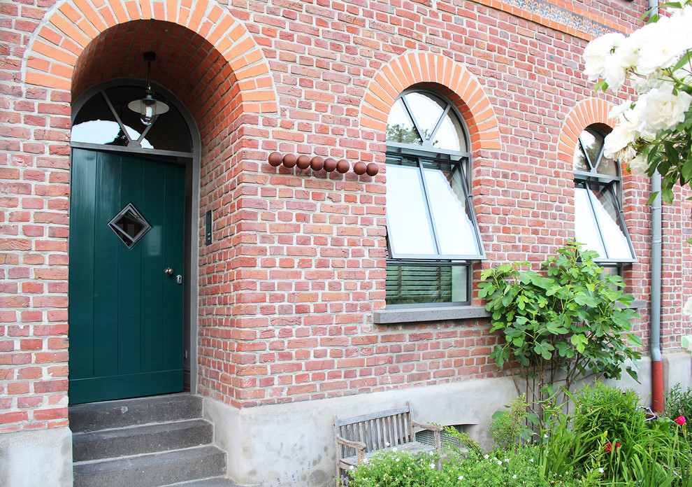 デュッセルドルフにある小さなカントリー風のおしゃれな玄関ドア (赤い壁、コンクリートの床、緑のドア、グレーの床) の写真