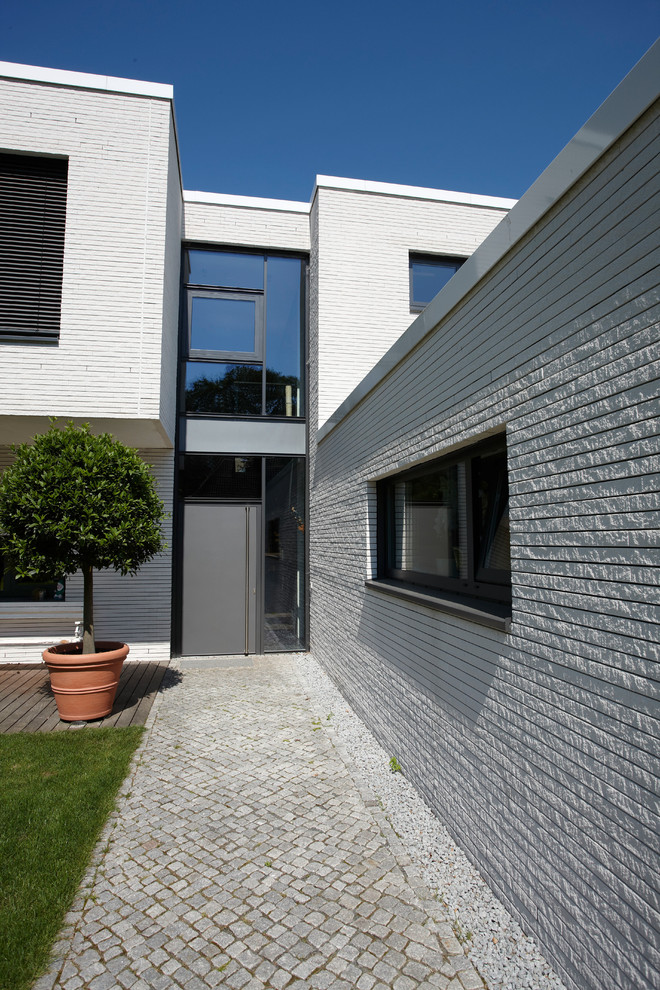 Réalisation d'une porte d'entrée design avec un mur blanc, une porte simple et une porte grise.
