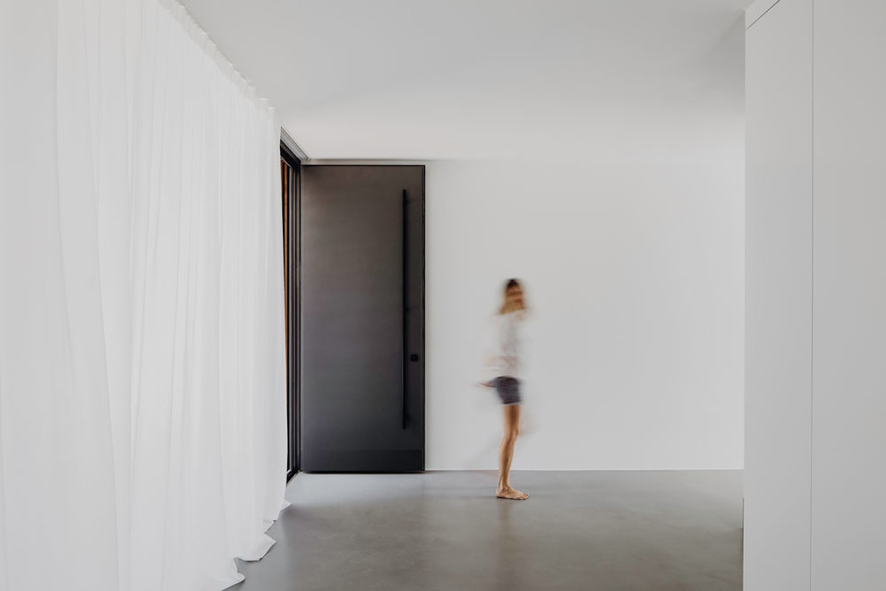 Exempel på en mycket stor modern foajé, med vita väggar, betonggolv, en enkeldörr, en svart dörr och grått golv