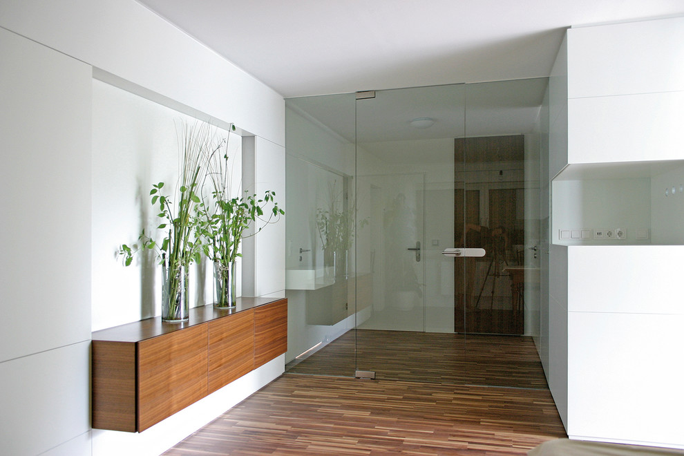 Modelo de vestíbulo actual de tamaño medio con paredes blancas, suelo de madera en tonos medios, puerta simple y puerta blanca