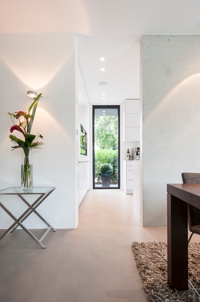 Imagen de entrada minimalista grande con paredes blancas, suelo de cemento, puerta simple, puerta de madera oscura y suelo gris