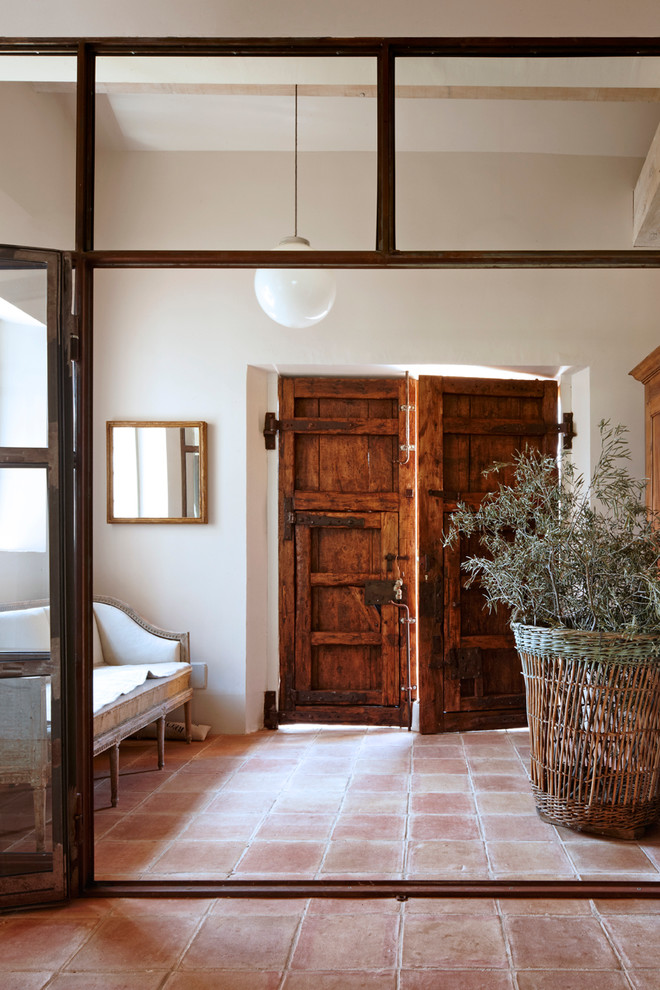 Exemple d'une entrée nature de taille moyenne avec un couloir, un mur blanc, tomettes au sol, une porte double et une porte en bois brun.