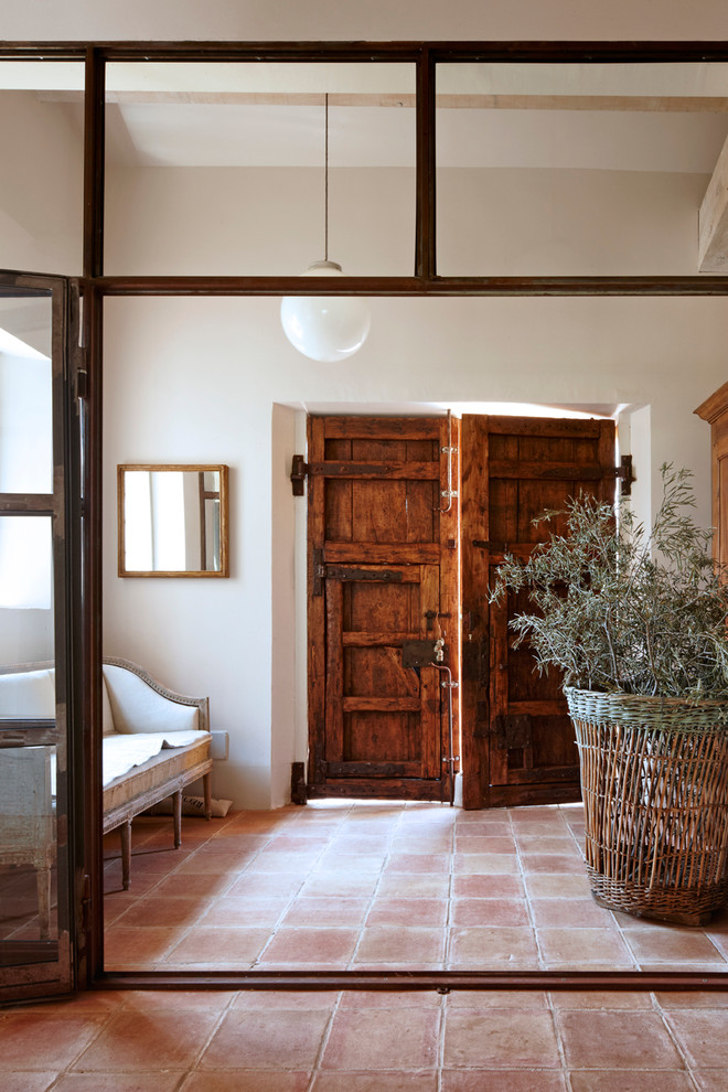 Diseño de distribuidor campestre de tamaño medio con paredes blancas, suelo de baldosas de terracota, puerta doble y puerta de madera en tonos medios