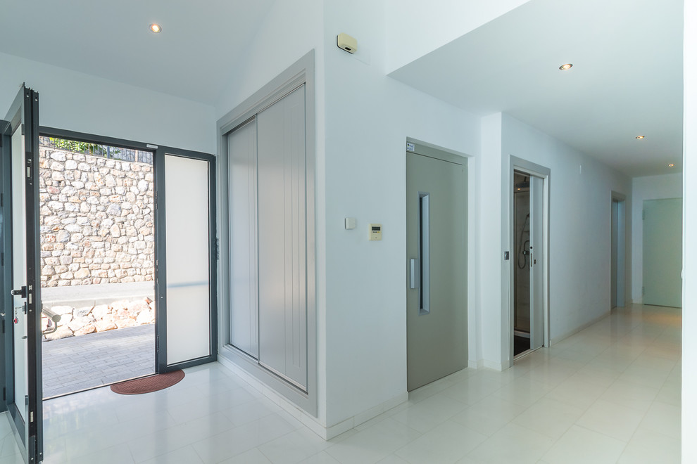 Exemple d'une grande entrée tendance avec un couloir, un mur blanc, un sol en marbre, une porte simple, une porte métallisée et un sol blanc.