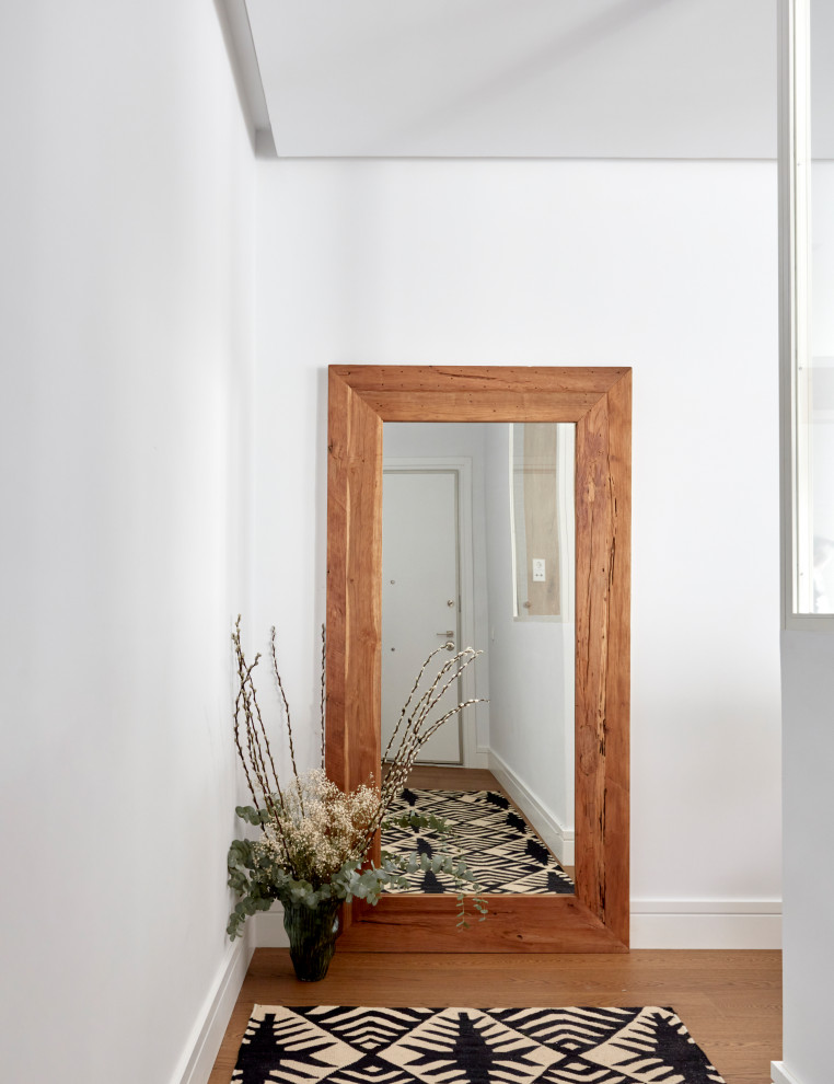 Cette photo montre une entrée éclectique de taille moyenne avec un couloir, un mur blanc, un sol en bois brun et une porte grise.