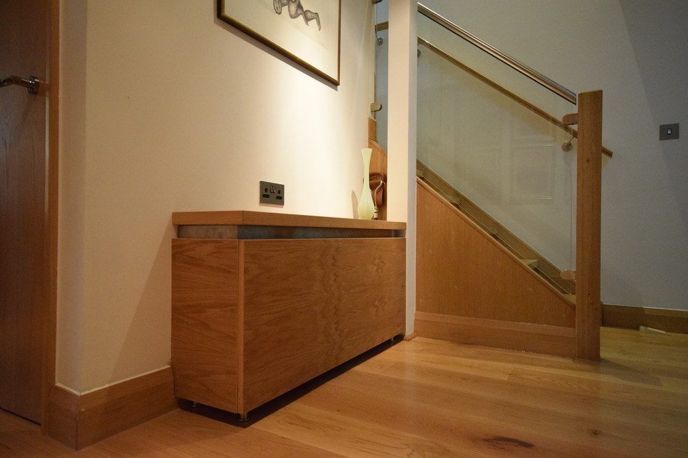 Cette image montre une petite entrée minimaliste avec un couloir, un mur blanc, un sol en bois brun et un sol marron.