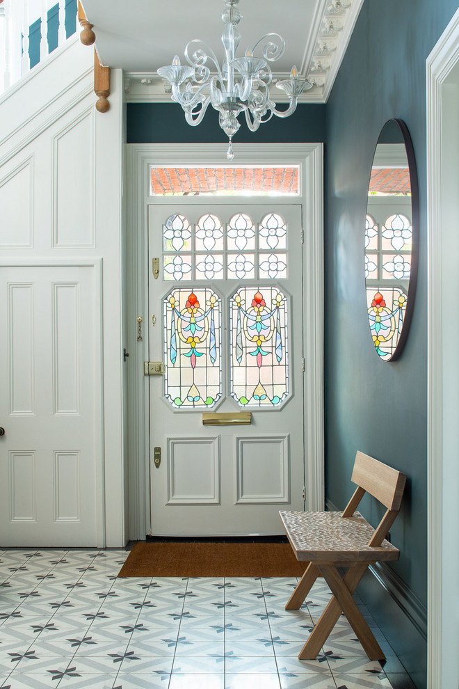 Klassisk inredning av en entré, med blå väggar, en enkeldörr, en vit dörr och flerfärgat golv