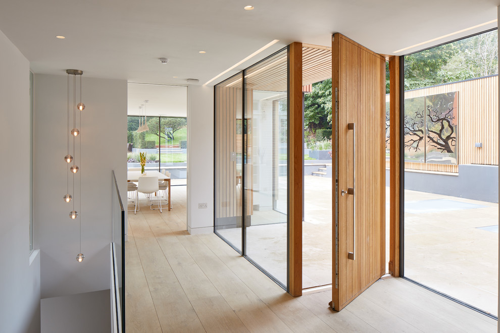 Ispirazione per un ingresso minimalista con pareti bianche, parquet chiaro, una porta a pivot, una porta in legno bruno e pavimento beige