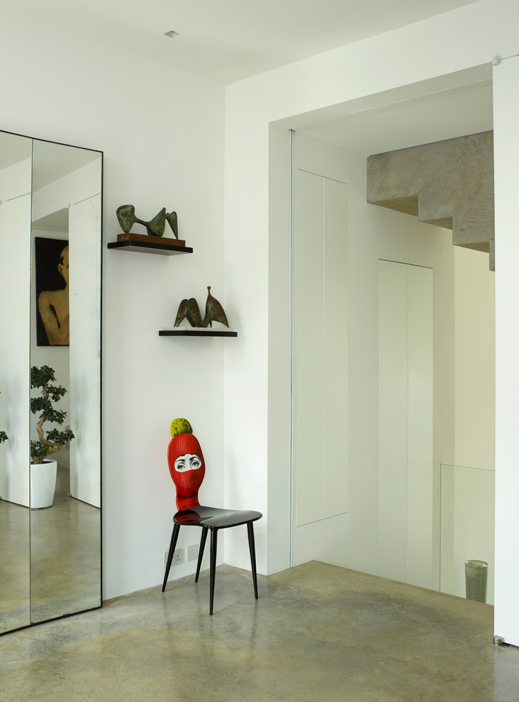 Photo of a large contemporary hallway in London with white walls, concrete flooring, a single front door, a black front door and grey floors.