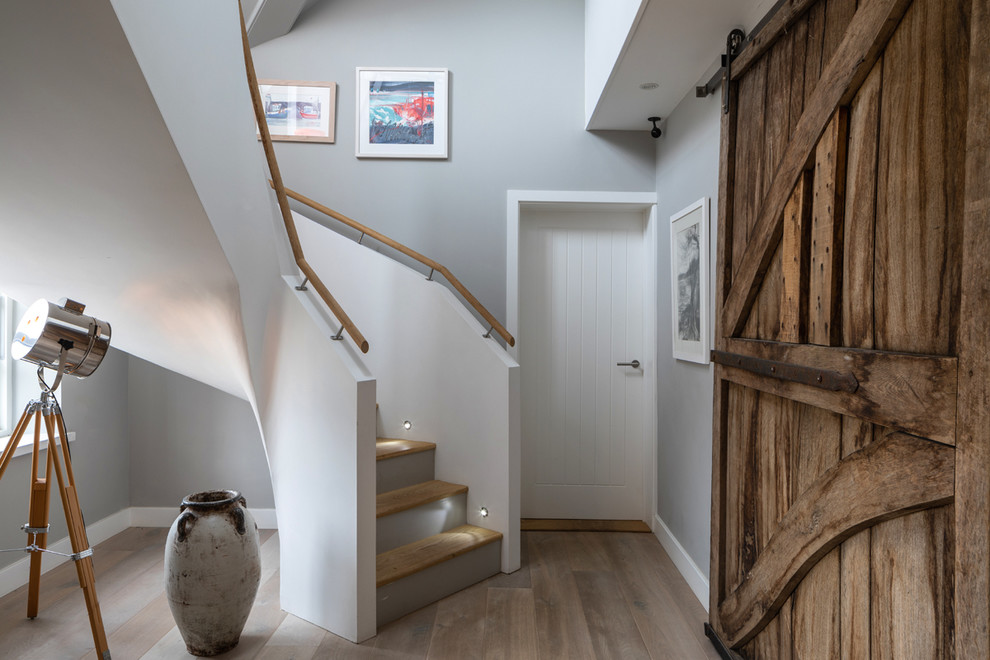 Diseño de hall costero grande con paredes grises, suelo de madera clara, puerta de madera en tonos medios, suelo gris y puerta simple