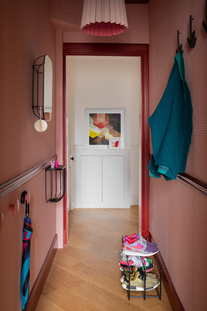 Cette image montre une petite entrée design avec un mur rose, un sol en bois brun, un couloir et un sol marron.