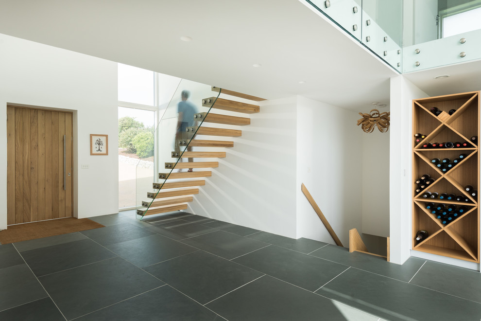This is an example of a medium sized contemporary foyer in Cornwall with white walls, slate flooring, a single front door, a light wood front door and grey floors.