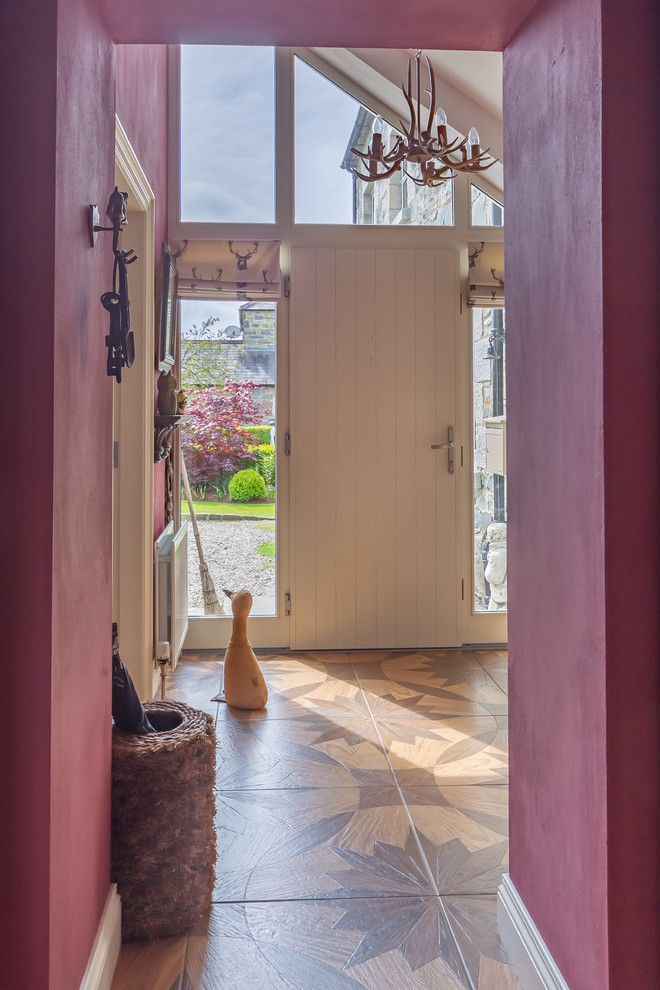 Lantlig inredning av en entré, med lila väggar, klinkergolv i keramik, en enkeldörr, en vit dörr och brunt golv