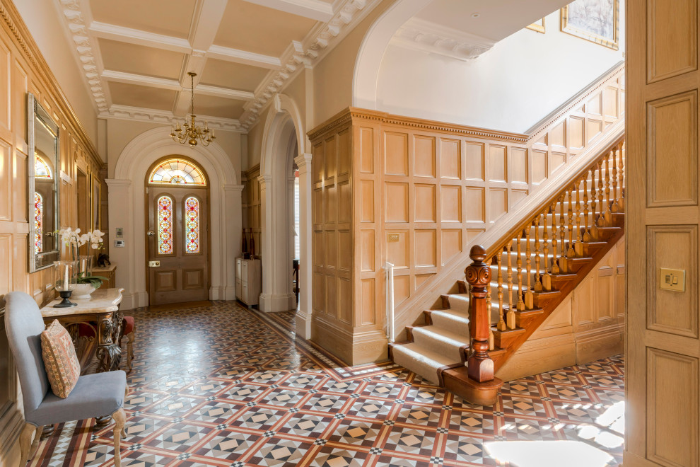 Exempel på en klassisk foajé, med beige väggar, en enkeldörr, mellanmörk trädörr och flerfärgat golv