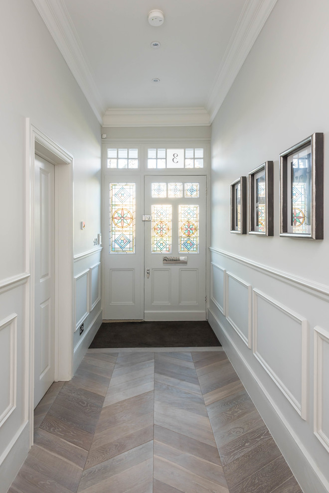 This is an example of an expansive modern front door in London with light hardwood flooring, white walls, a single front door and a white front door.