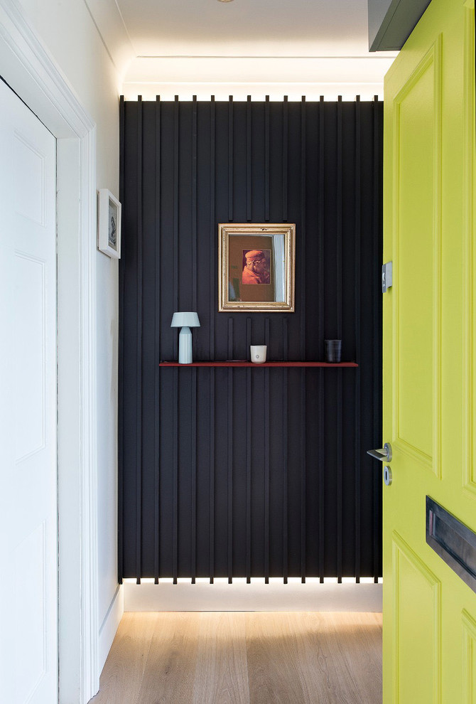 Modern inredning av en entré, med svarta väggar, ljust trägolv, en enkeldörr, en gul dörr och beiget golv