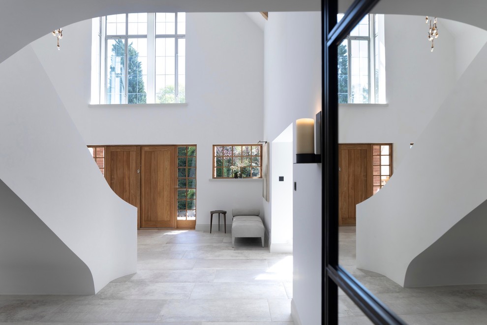 Modern inredning av en mycket stor hall, med vita väggar, klinkergolv i porslin, en dubbeldörr, ljus trädörr och vitt golv