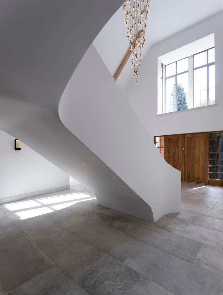 チェシャーにあるラグジュアリーな巨大なコンテンポラリースタイルのおしゃれな玄関ホール (白い壁、磁器タイルの床、淡色木目調のドア、白い床) の写真