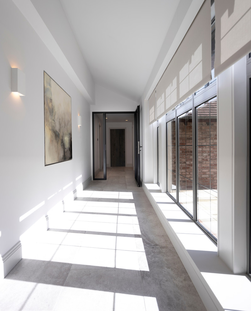 Cette image montre une très grande entrée design avec un couloir, un mur blanc, un sol en carrelage de porcelaine, une porte double, une porte en bois clair et un sol blanc.
