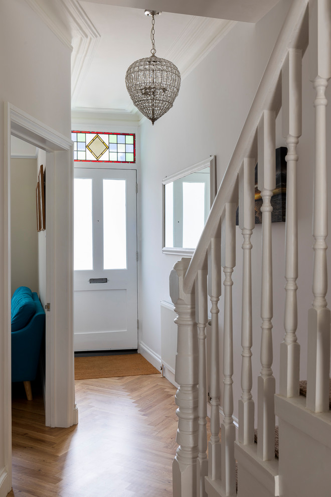Diseño de puerta principal clásica pequeña con paredes blancas, suelo de madera oscura, puerta simple, puerta de madera clara y suelo marrón