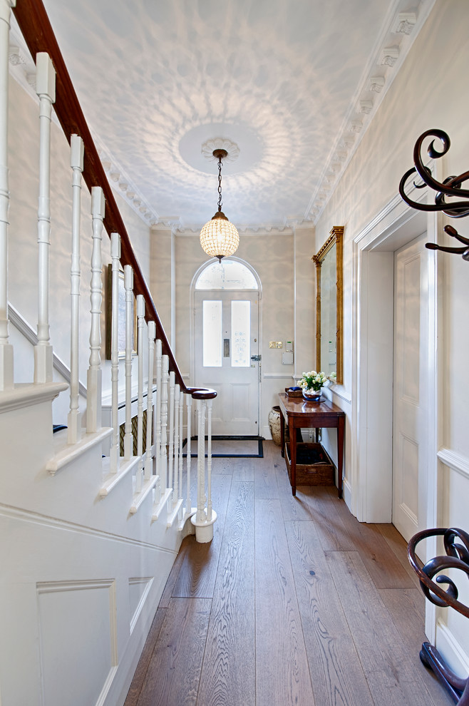 Mid-sized elegant medium tone wood floor entryway photo in London with a white front door and white walls