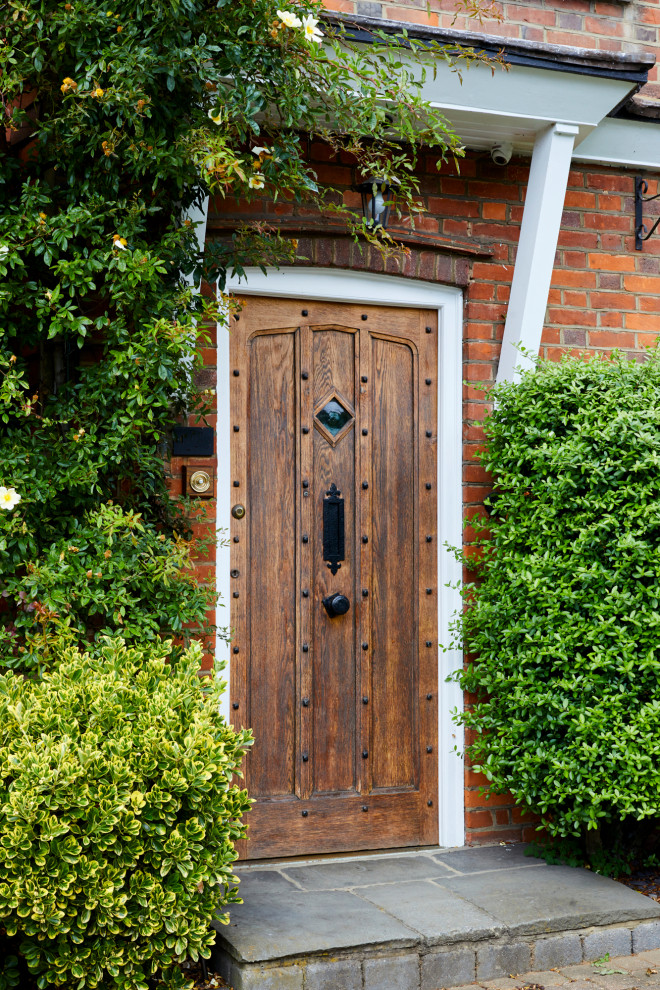 Imagen de puerta principal clásica de tamaño medio con paredes rojas, suelo de cemento, puerta simple, puerta marrón, suelo gris y ladrillo