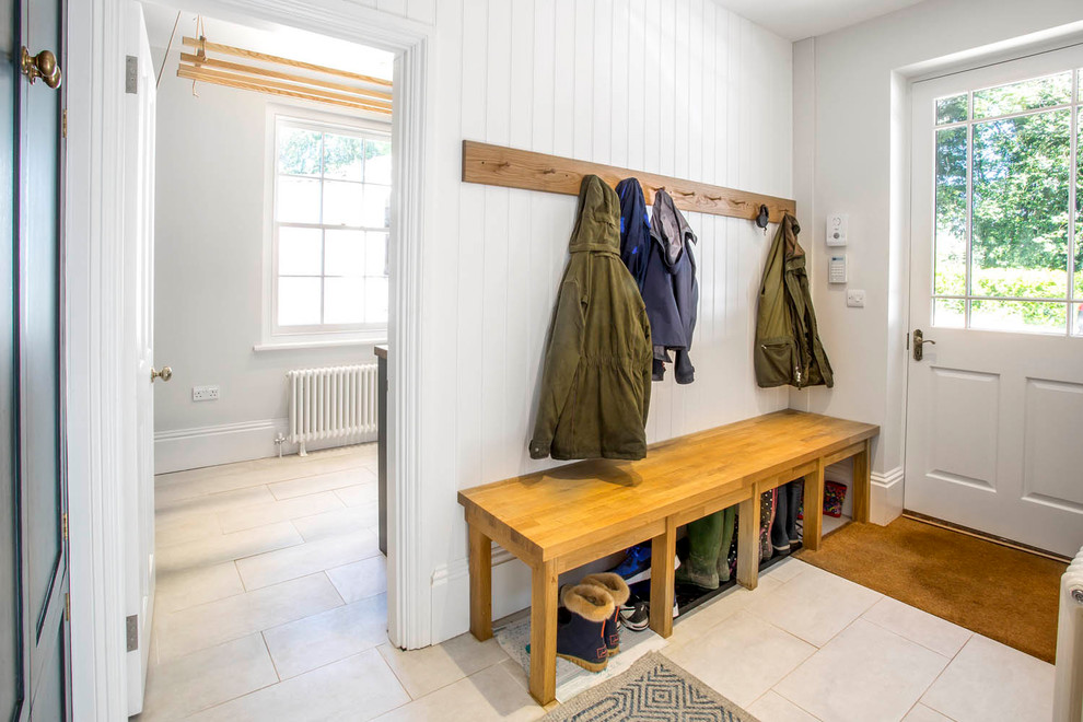 This is an example of a medium sized farmhouse boot room in Berkshire with white walls, travertine flooring, a white front door and beige floors.