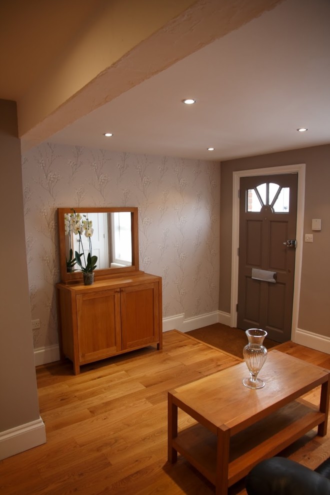 Cette photo montre une entrée tendance de taille moyenne avec un couloir, un mur gris, un sol en bois brun, une porte simple, une porte grise et un sol marron.
