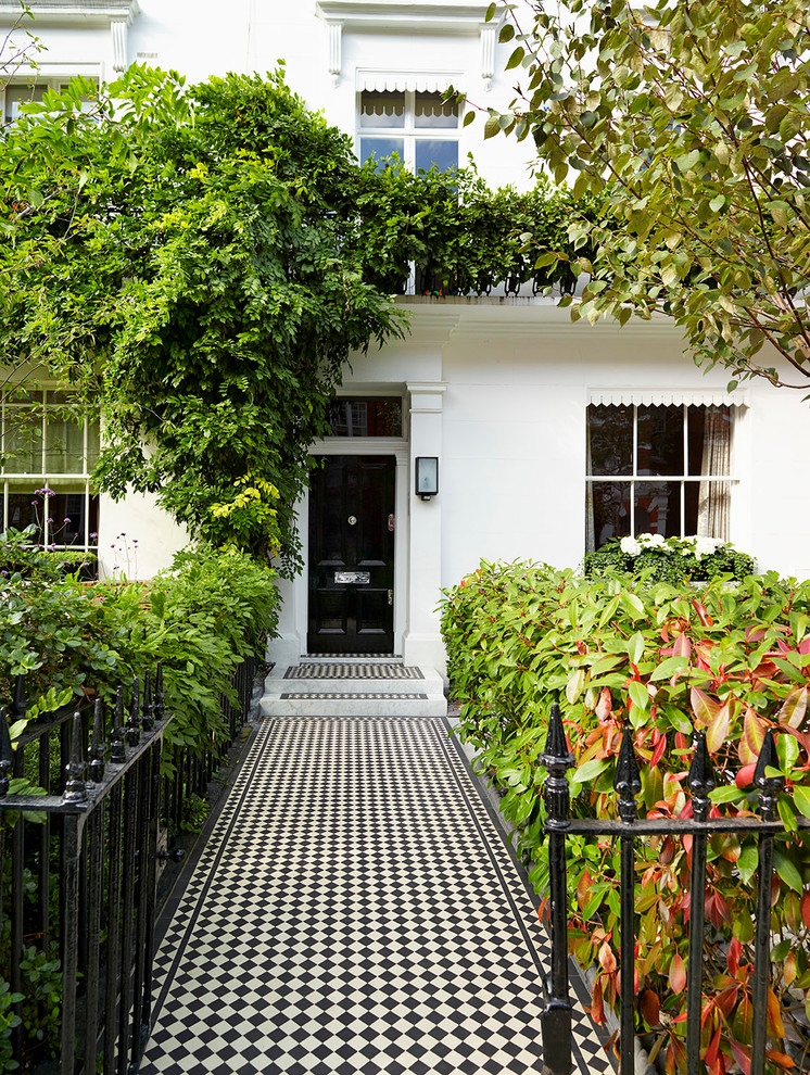 Example of a large classic ceramic tile entryway design in London with a black front door and white walls