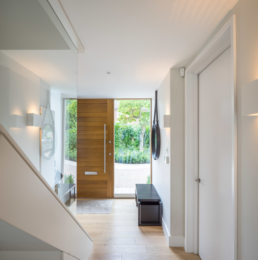 Cette image montre une entrée design avec parquet clair, un mur gris, une porte simple et une porte en bois brun.