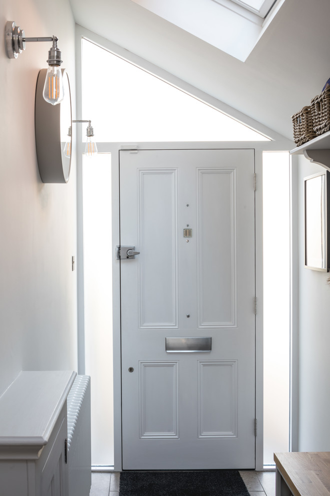 Bild på en liten funkis foajé, med vita väggar, klinkergolv i porslin, en enkeldörr, en vit dörr och grått golv