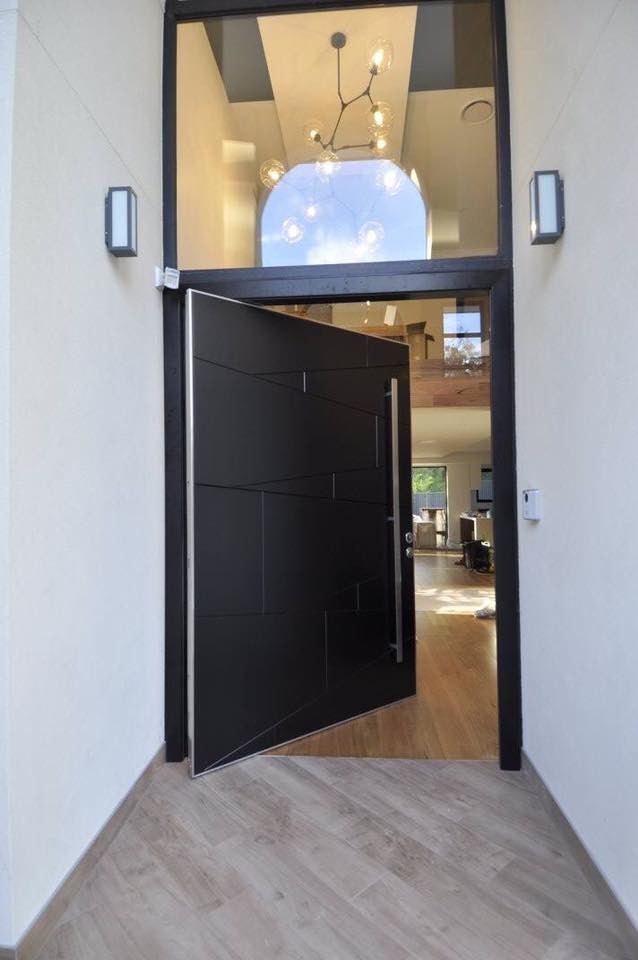 Modelo de puerta principal moderna extra grande con paredes blancas, suelo de madera oscura y puerta pivotante