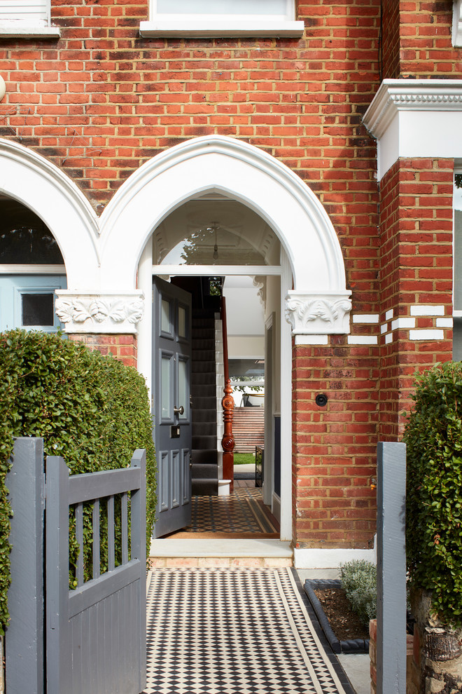 ロンドンにある高級な広いヴィクトリアン調のおしゃれな玄関ドア (グレーのドア、磁器タイルの床、マルチカラーの床、レンガ壁) の写真