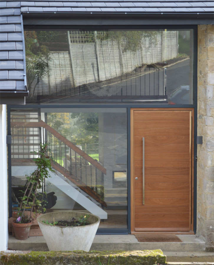 Cette photo montre une grande porte d'entrée tendance avec un mur blanc, sol en béton ciré, une porte pivot et une porte en bois brun.