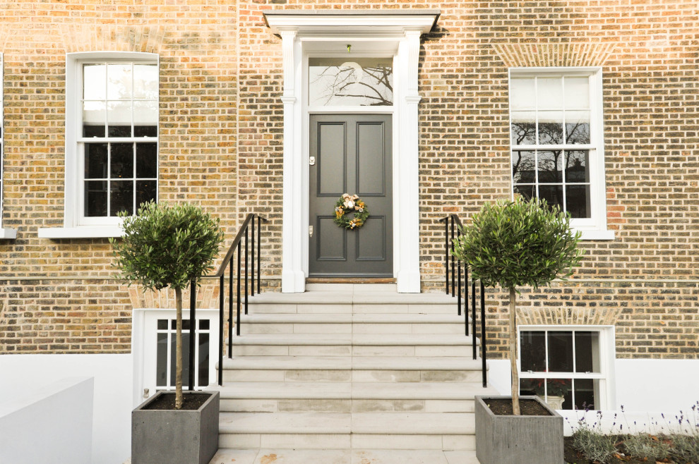 Inspiration for a large timeless brick wall single front door remodel in London with a gray front door and brown walls