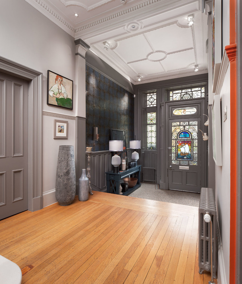 Стильный дизайн: фойе: освещение в стиле фьюжн с серыми стенами, паркетным полом среднего тона, одностворчатой входной дверью, серой входной дверью и коричневым полом - последний тренд